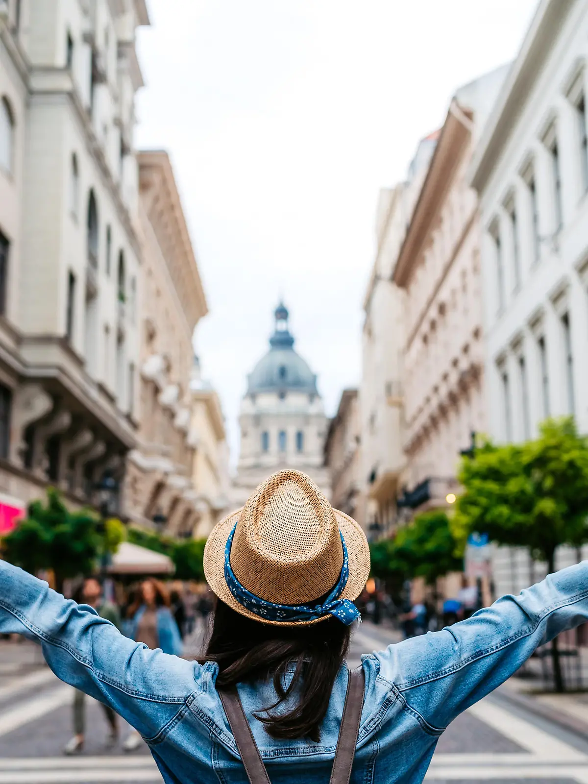 Young female tourist standing with outstretched arms on Budapest street, rear view.
