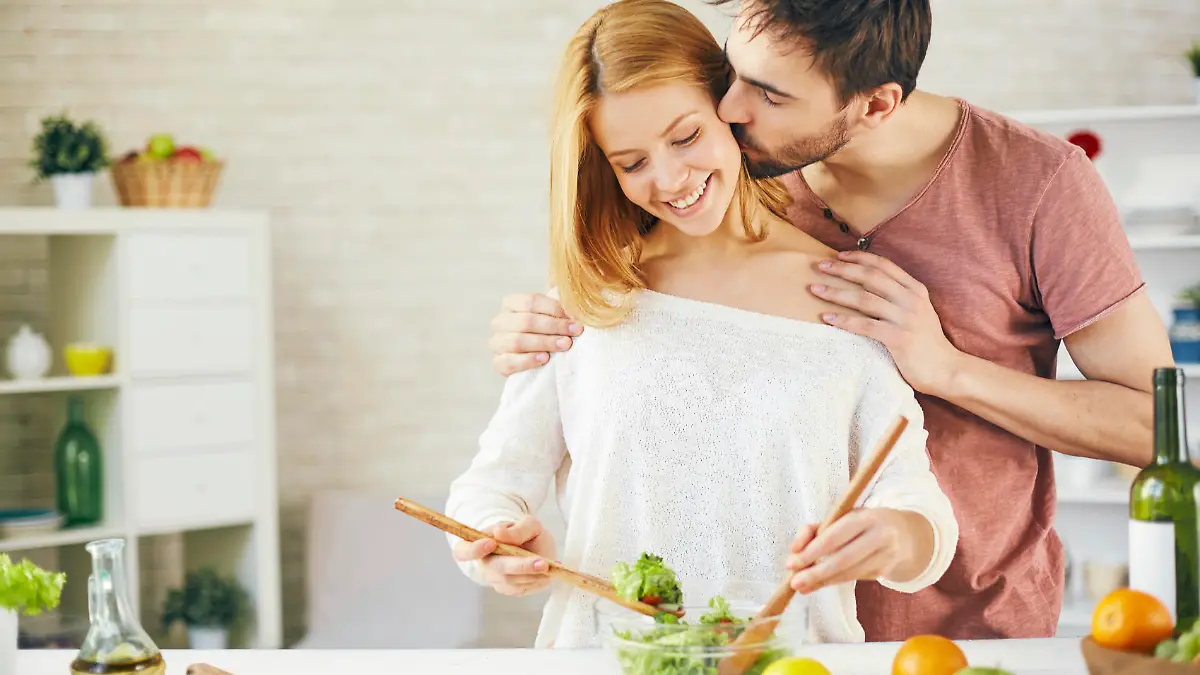 Affectionate young man kissing his wife while she cooking salad