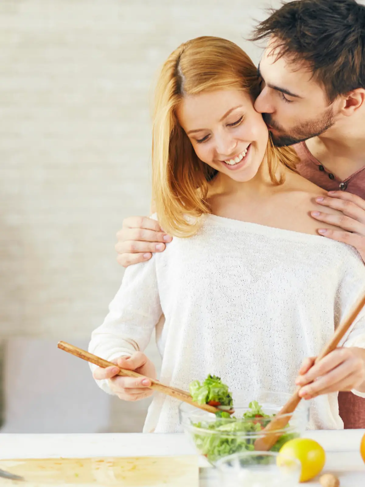 Affectionate young man kissing his wife while she cooking salad