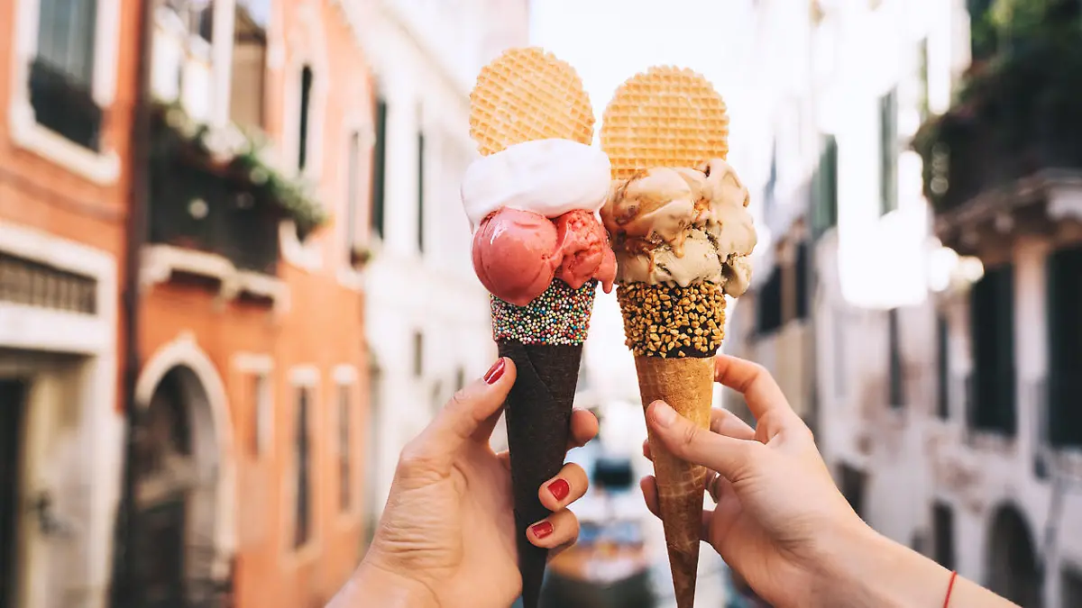Beautiful and delicious italian gelato in waffle cone in front of streets and bridges of Venice. Ice cream in girls hands on background of water canal and historic buildings of Italy. Travel Europe.