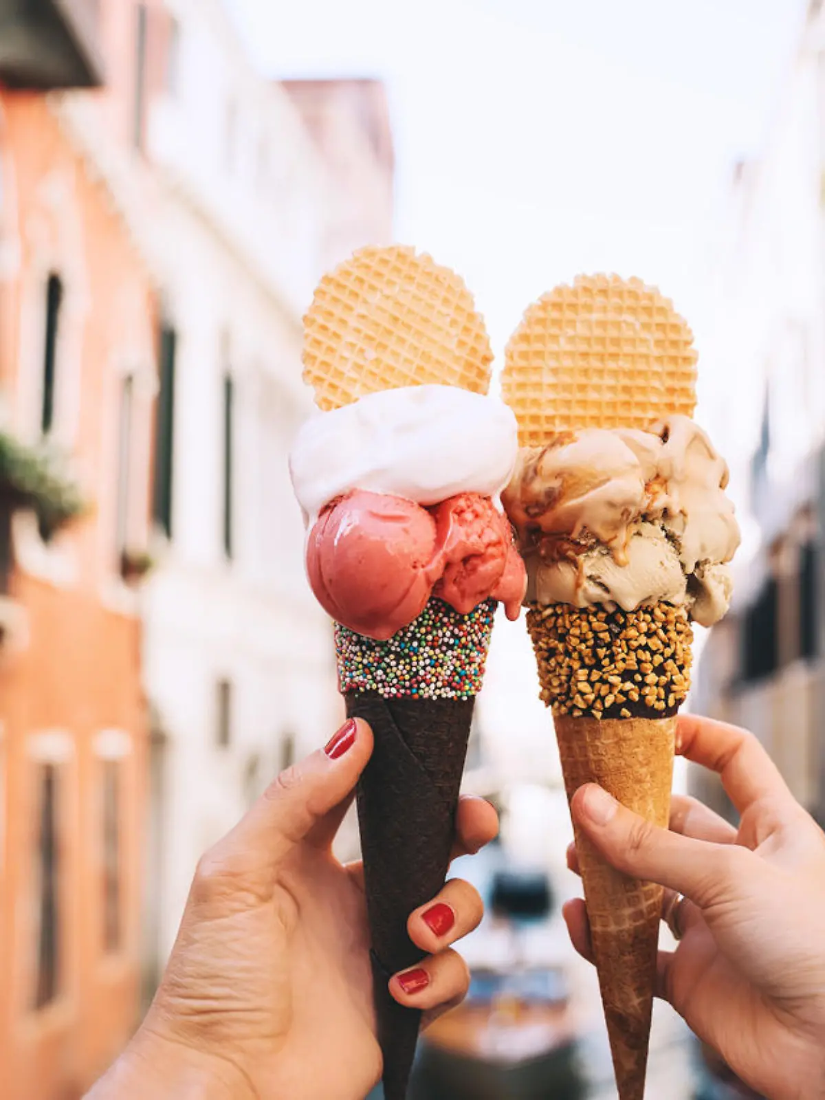 Beautiful and delicious italian gelato in waffle cone in front of streets and bridges of Venice. Ice cream in girls hands on background of water canal and historic buildings of Italy. Travel Europe.