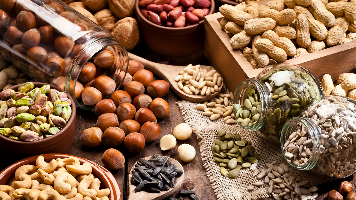 Horizontal shot of a rustic wood table filled with a large assortment of nuts like pistachios, hazelnut, pine nut, almonds, pumpkin seeds, sunflower seeds, peanuts, cashew and walnuts. Some nuts are in brown bowls and others in glass jars. Predominant color is brown. DSRL studio photo taken with Canon EOS 5D Mk II and Canon EF 100mm f/2.8L Macro IS USM