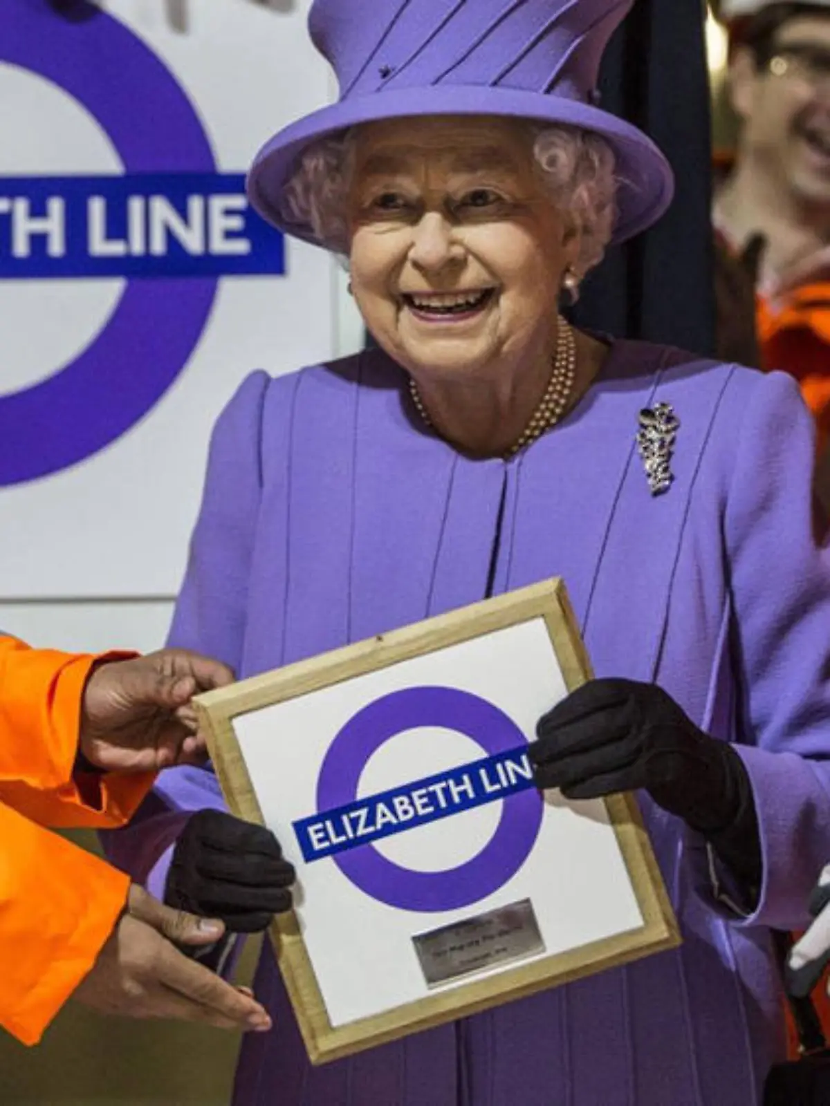 Stolz hält Queen Elizabeth II das Schild der neuen U-Bahn-Linie mit ihrem Namen hoch