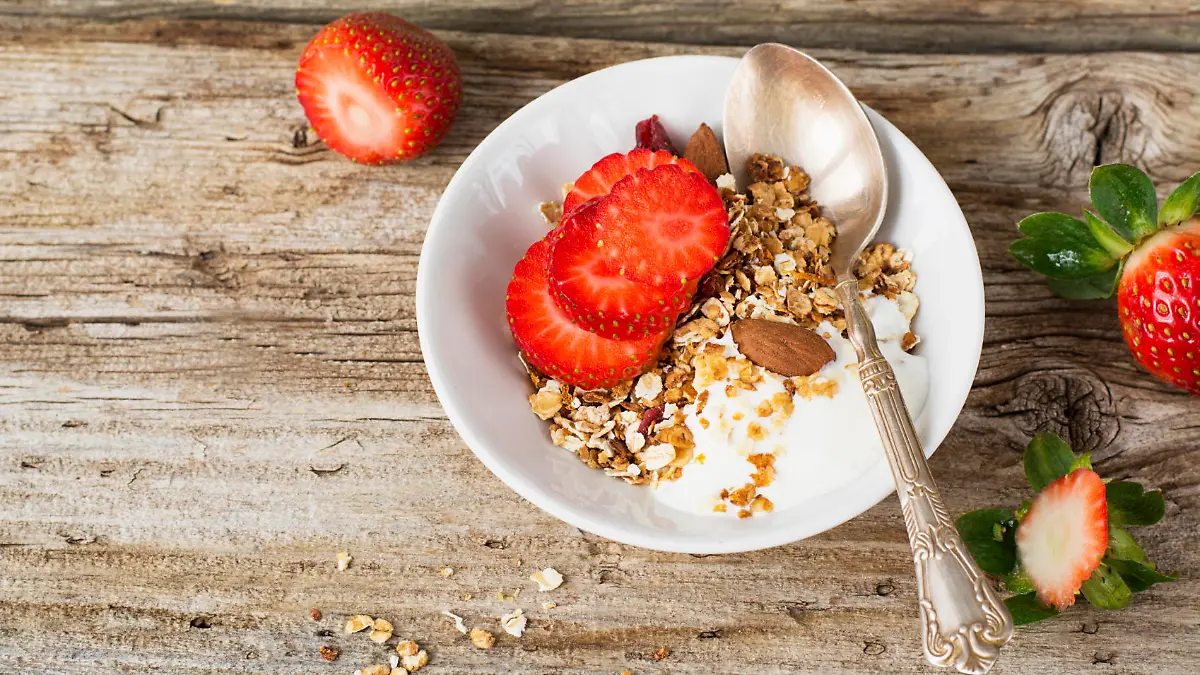 Home crunchy granola with fresh milk and strawberry slices on a simple wooden background. Concept of healthy food simple home. selective Focus