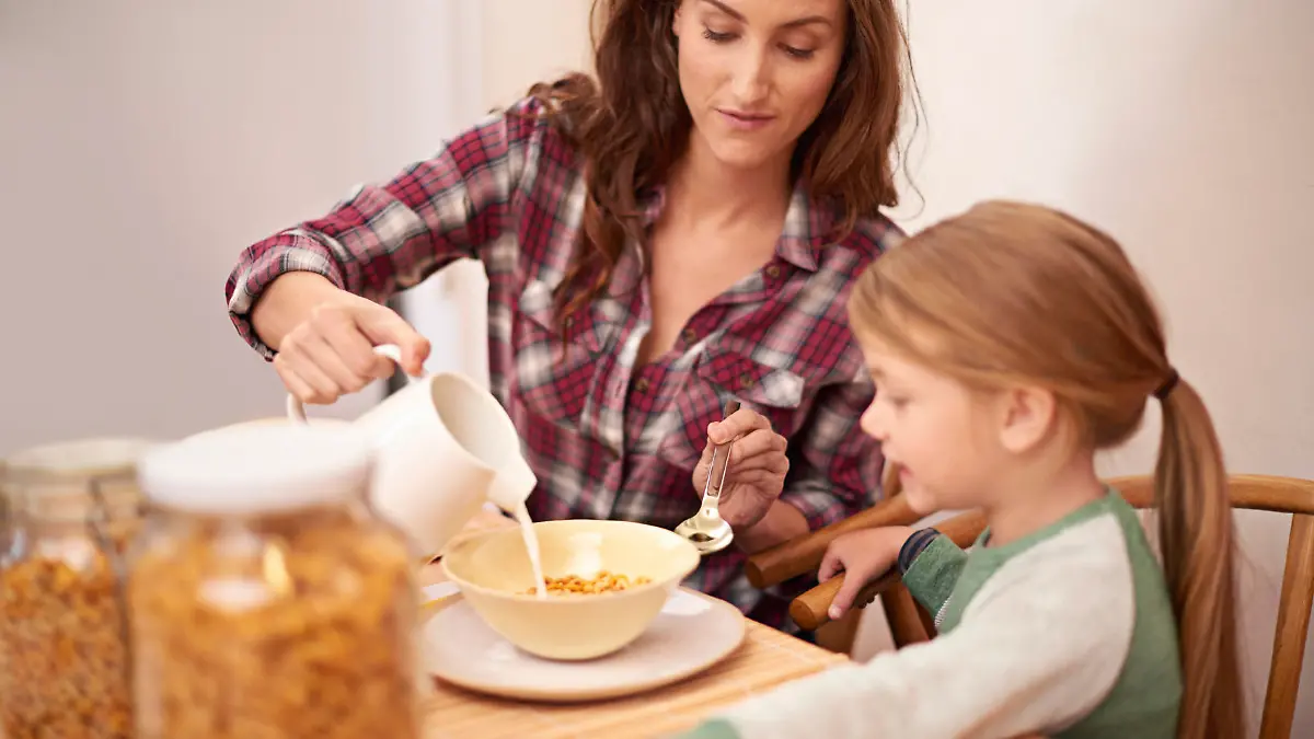Shot of a woman pouring milk over her daughter's cereal at breakfast time