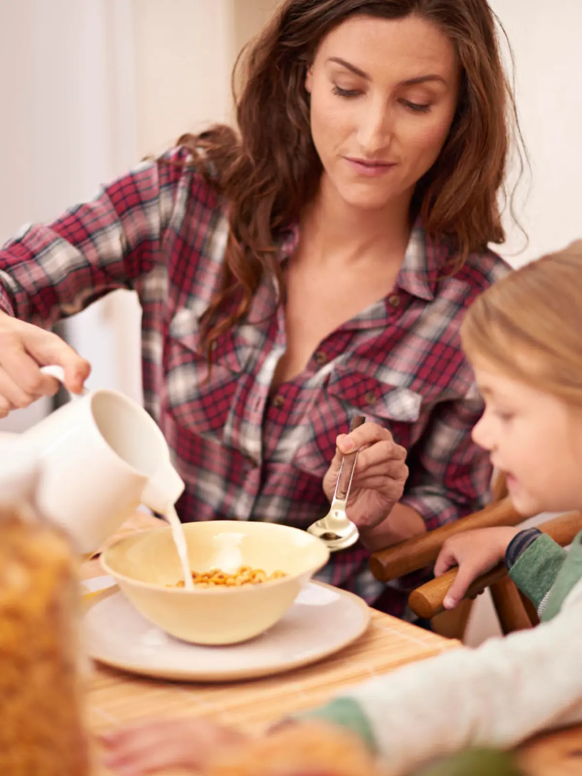 Shot of a woman pouring milk over her daughter's cereal at breakfast time