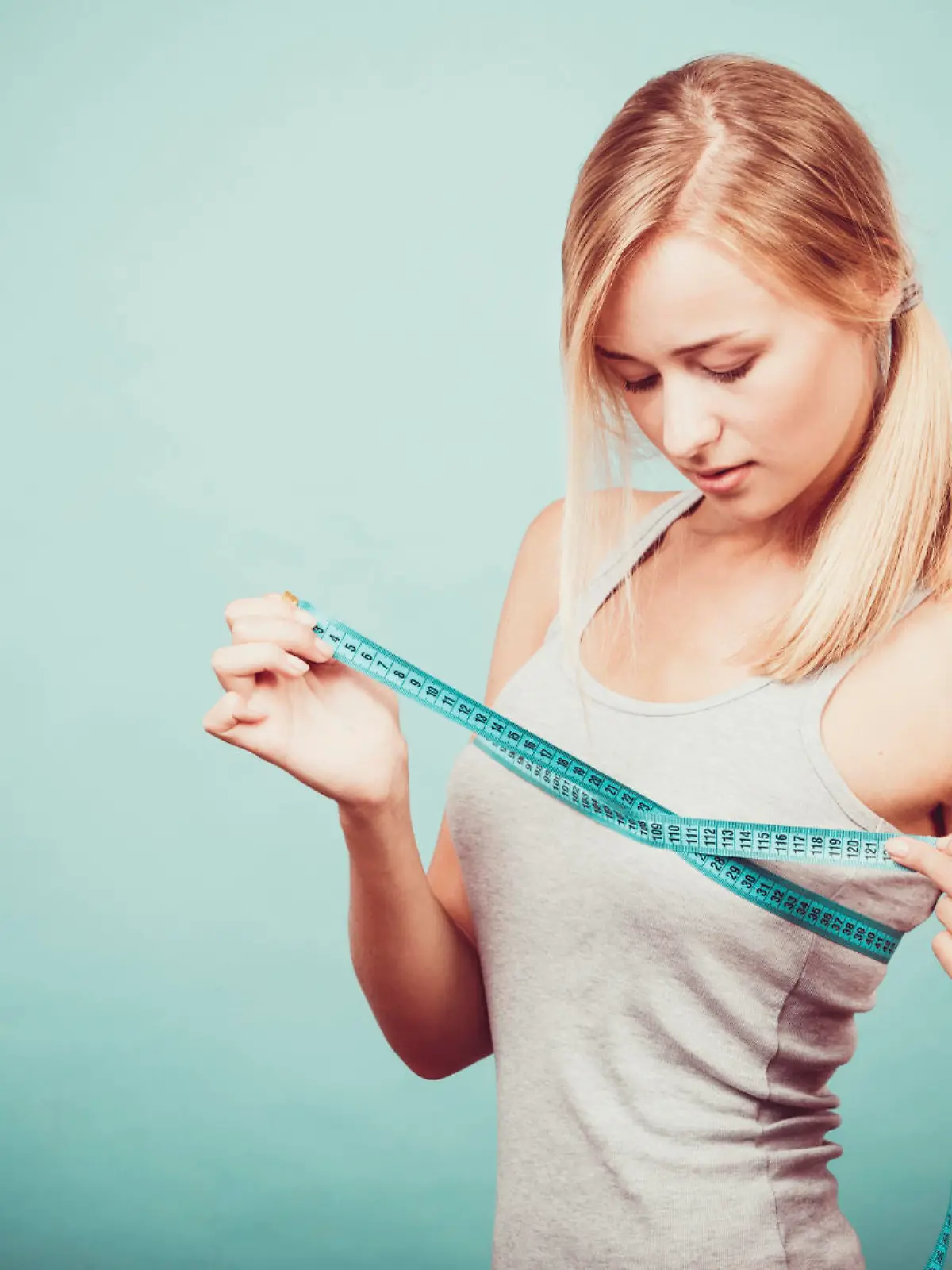 Fitness woman fit girl in sportswear with measure tape measuring her size chest breast on blue