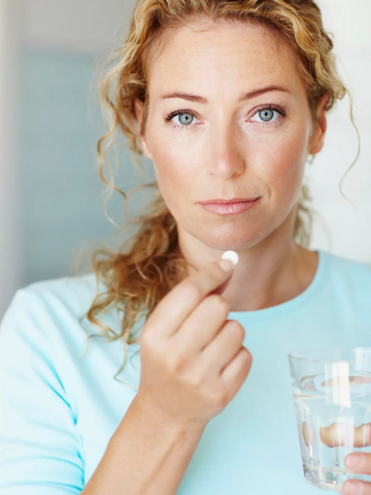 Portrait of a woman about to take some pain medication with a glass of water