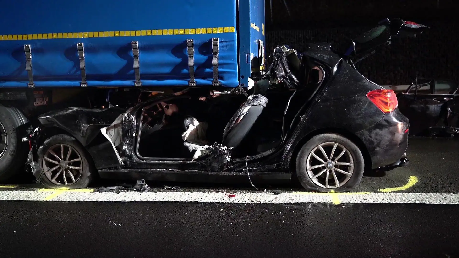 Der zertrümmerte Unfallwagen klemmt unter dem Lkw