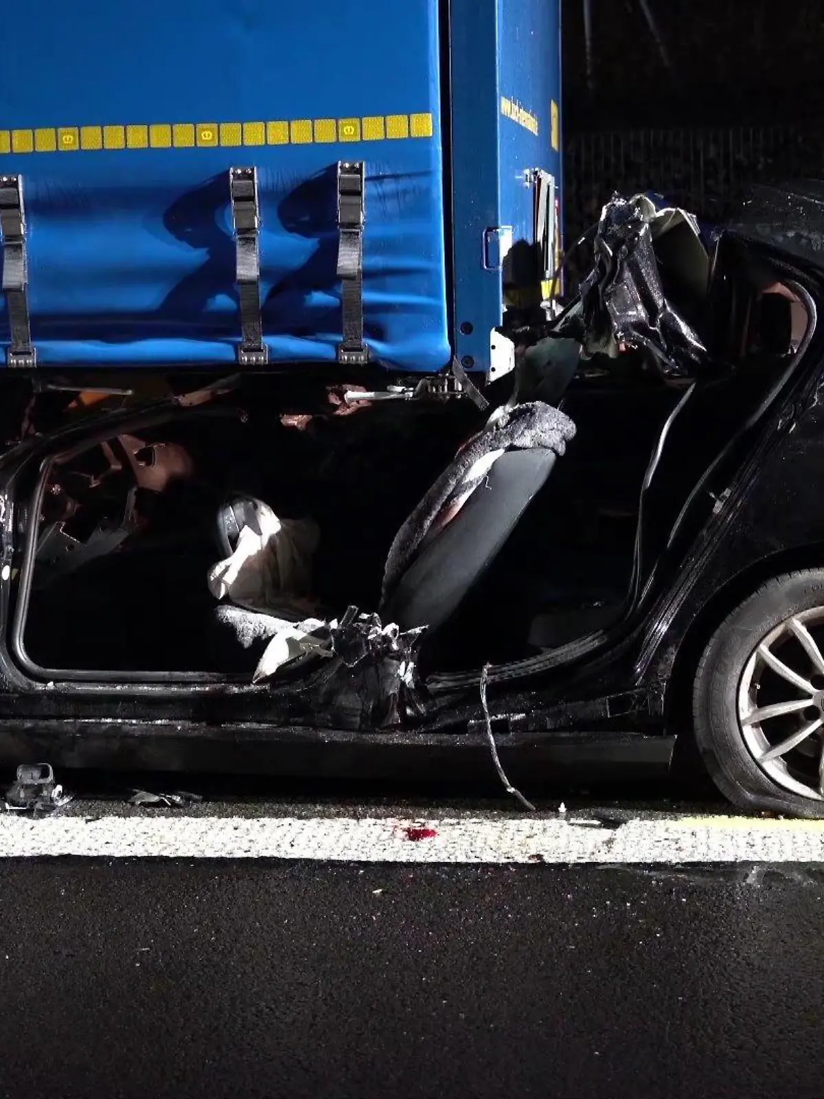 Der zertrümmerte Unfallwagen klemmt unter dem Lkw