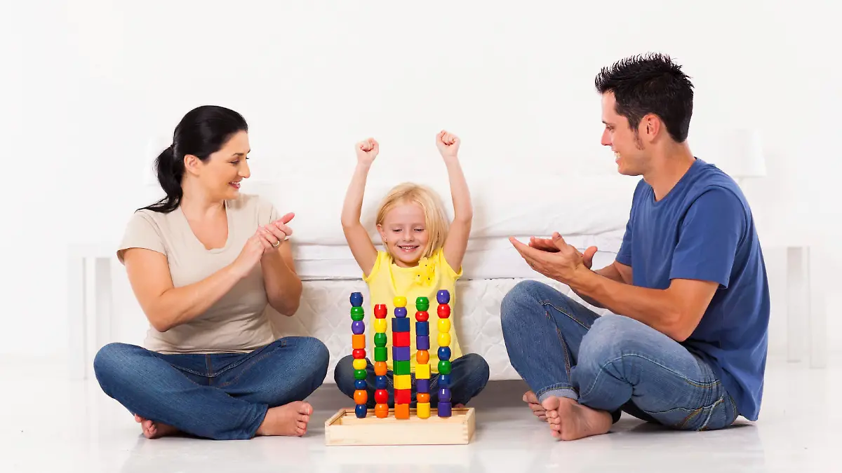 happy little girl playing toys with parents on bedroom floor