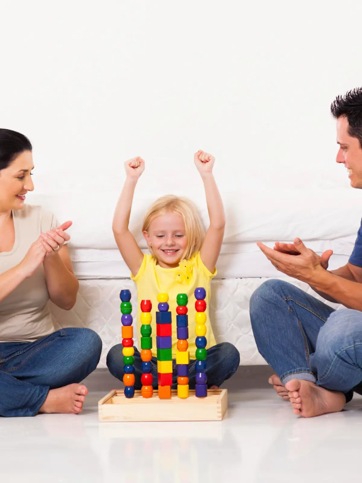happy little girl playing toys with parents on bedroom floor