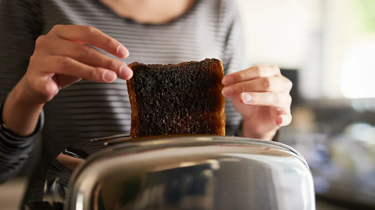 Cropped shot of a woman removing a slice of burnt toast from a toaster at home