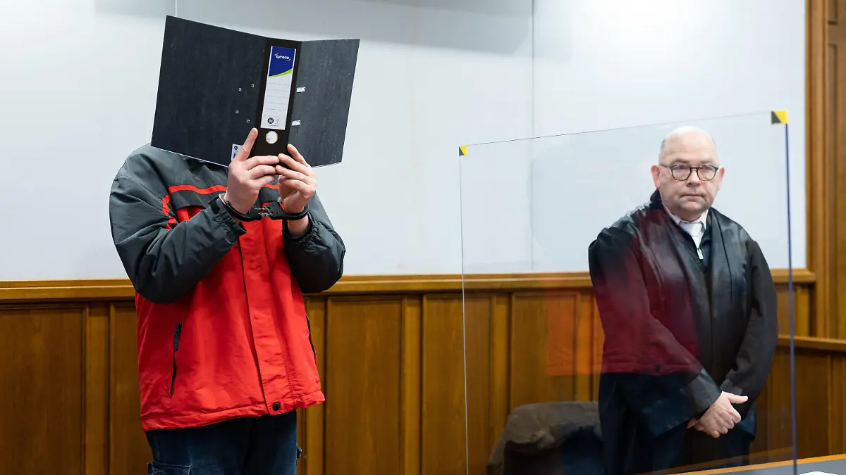 19.01.2023, Niedersachsen, Bückeburg: Der Angeklagte steht vor Beginn der Gerichtsverhandlung in einem Gerichtssaal im Landgericht Bückeburg und hält sich einen Aktenordner vor sein Gesicht. Daneben steht sein Verteidiger Michael Einars (r). Am 19.01.2023 wird die Urteilsverkündung erwartet. Dem Angeklagten wird vorgeworfen, im Juni 2022 in Obernkirchen die Geschäftsinhaberin von einem Schreibwarengeschäft getötet zu haben. Foto: Michael Matthey/dpa +++ dpa-Bildfunk +++