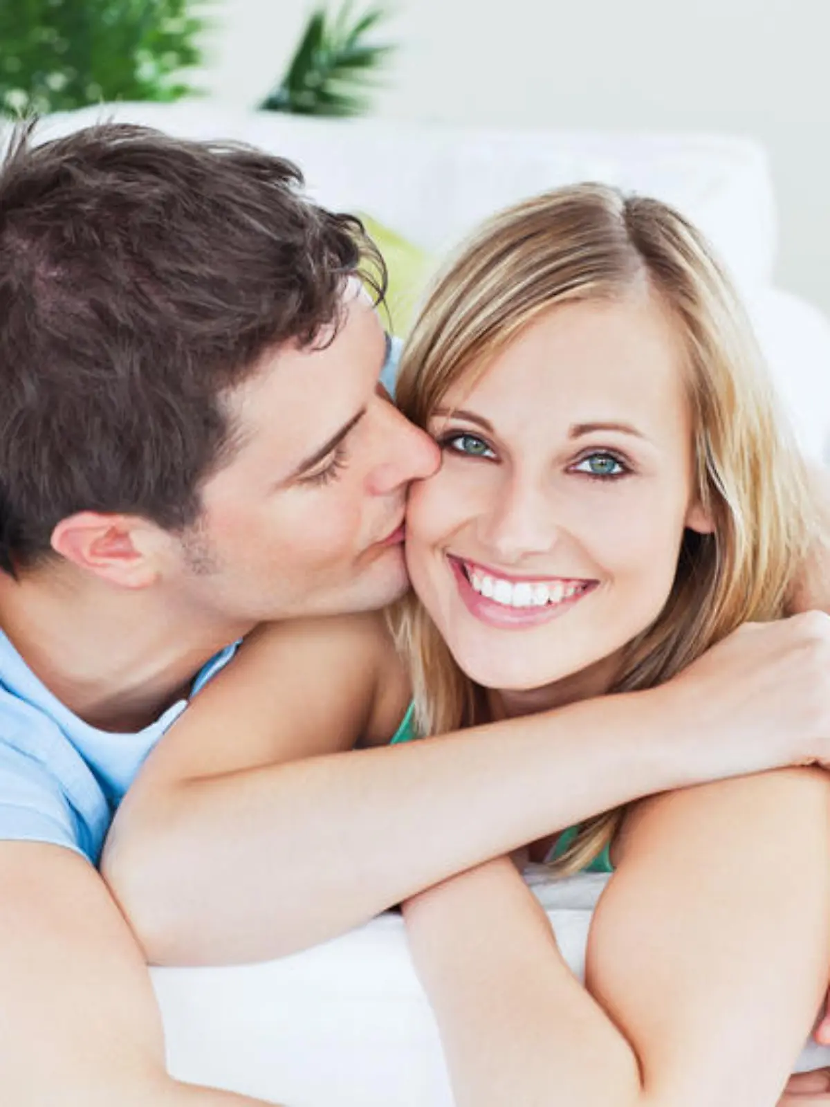 Portrait of an attentive boyfriend kissing his smiling girlfriend relaxing in the living-room