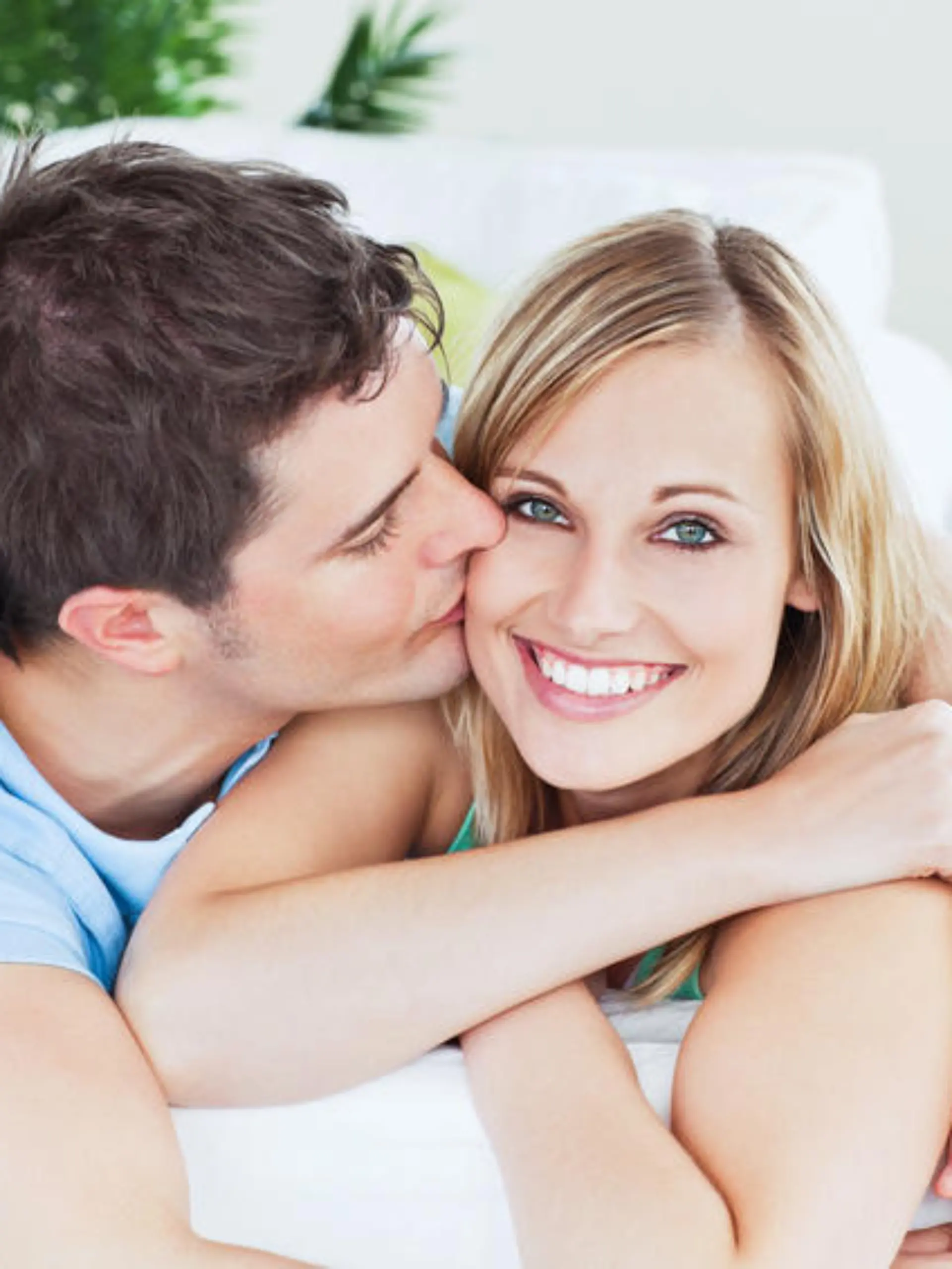 Portrait of an attentive boyfriend kissing his smiling girlfriend relaxing in the living-room