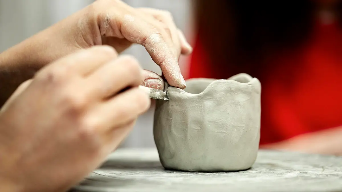 Cropped image of artist's hands making cup with clay on pottery wheel. Woman is working in pottery workshop. Potter is making art product at studio.