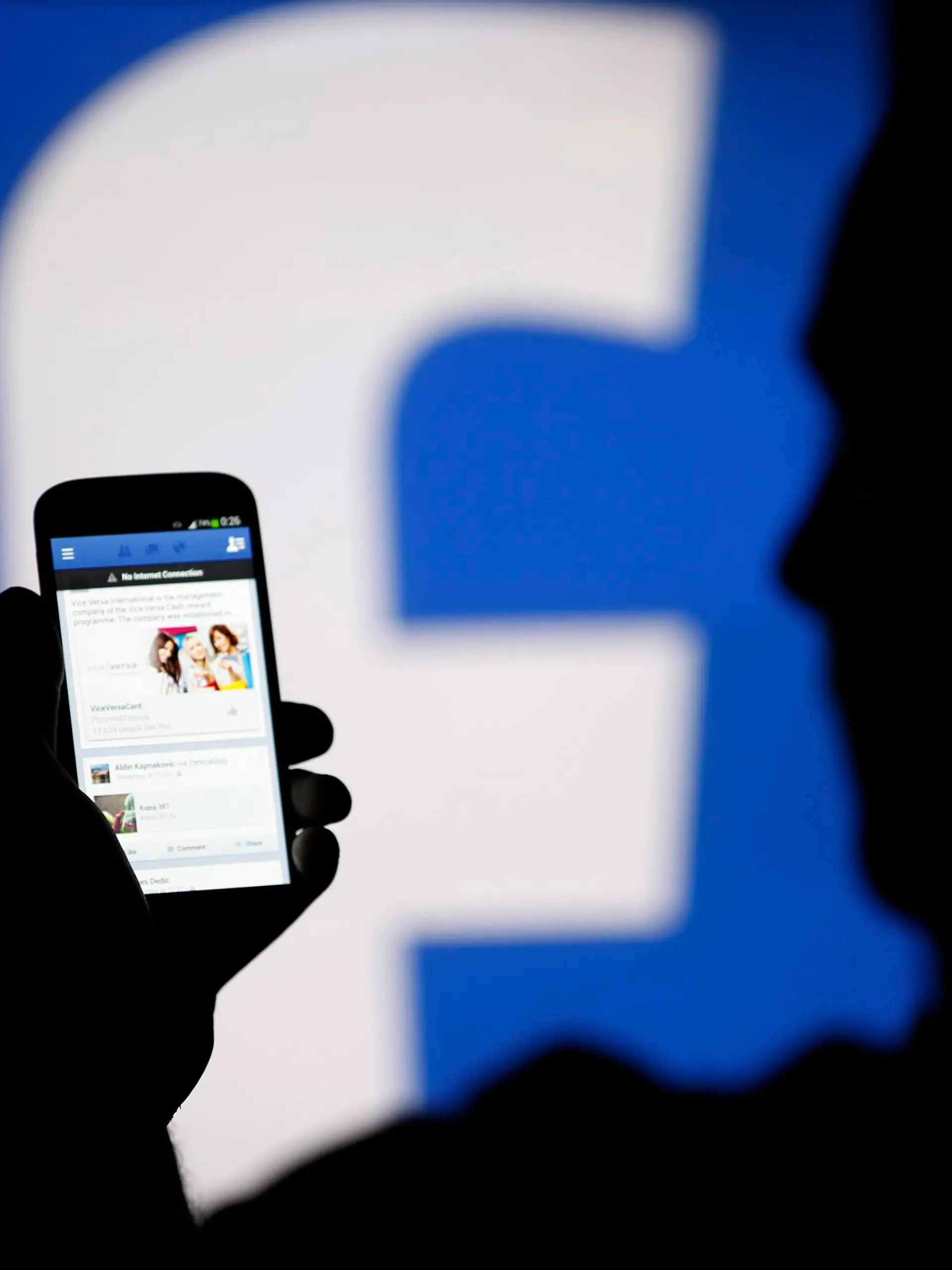 A man is silhouetted against a video screen with an Facebook logo as he poses with an Samsung smartphone in this photo illustration taken in the central Bosnian town of Zenica in a file photo taken August 14, 2013.  Facebook Inc will buy fast-growing mobile-messaging startup WhatsApp for $19 billion in cash and stock, as the world's largest social network looks for ways to boost its popularity, especially among a younger crowd. REUTERS/Dado Ruvic/Files   (BOSNIA AND HERZEGOVINA - Tags: BUSINESS TELECOMS)