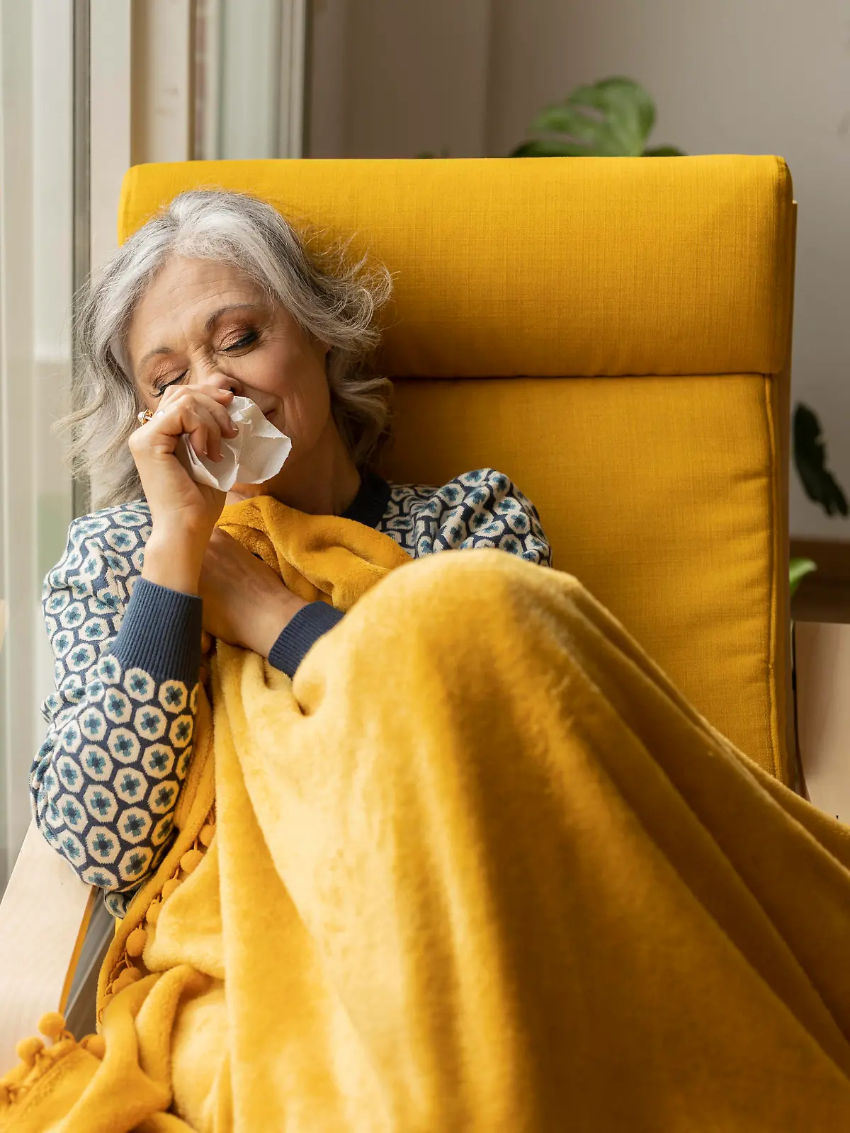 Mature woman with tissue blowing nose by window at home model released, Symbolfoto property released, JCCMF10163