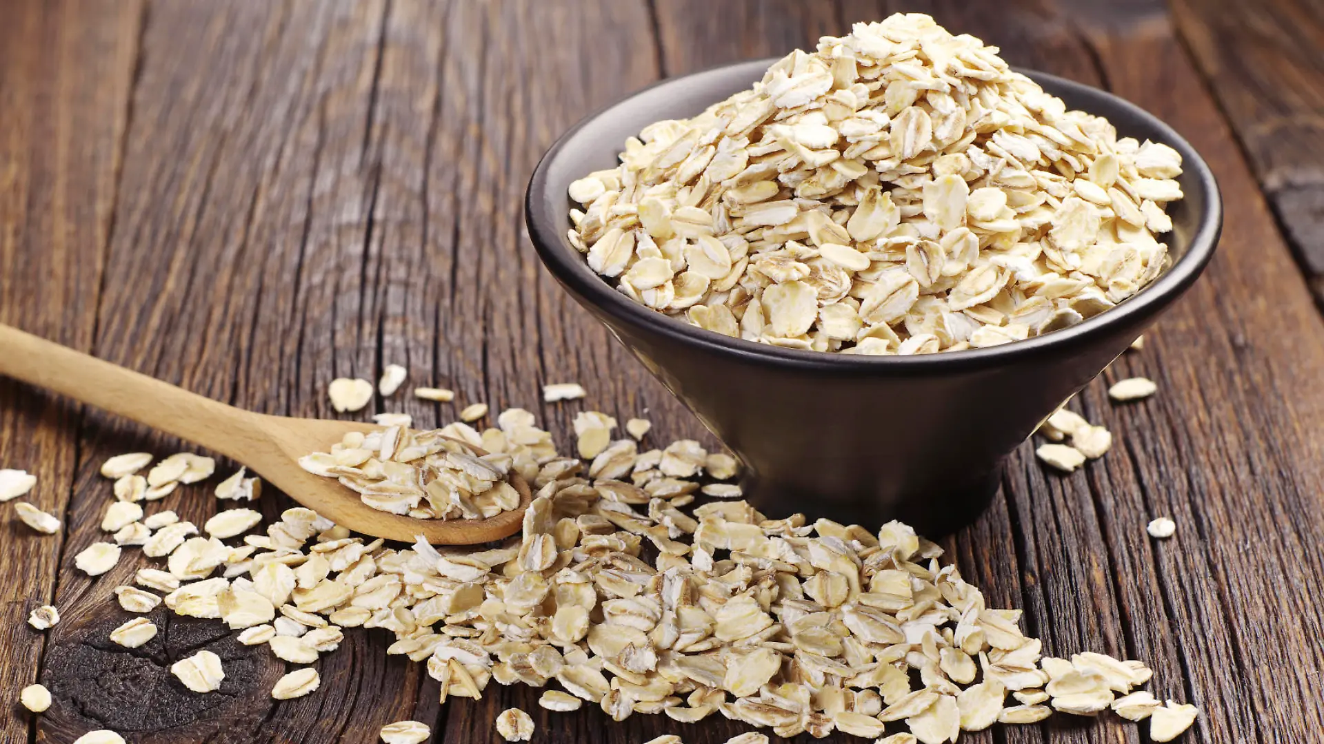 Oatmeal or oat flakes in black bowl and near on dark wooden table