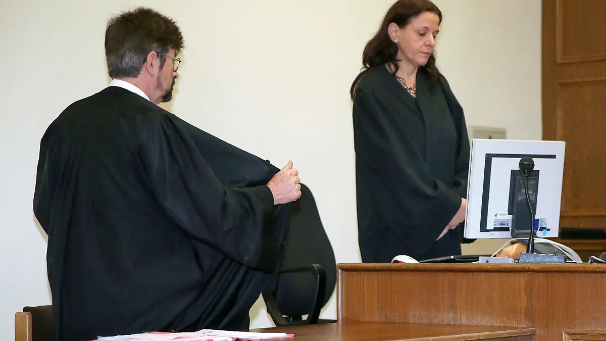 Der Anwalt Gerd-M. Achterberg schirmt am 08.10.2015 in Hamburg vor der erwarteten Urteilsverkündung im Gerichtssaal die Angeklagte Marie mit seiner Robe vor Blicken ab. (Rechts im Bild die Gerichtsschreiberin). Im Prozess gegen eine Mutter wegen Misshandlung ihres Kindes mit verseuchten Spritzen wird das Urteil vor dem Hamburger Landgericht erwartet. Foto: Axel Heimken/dpa