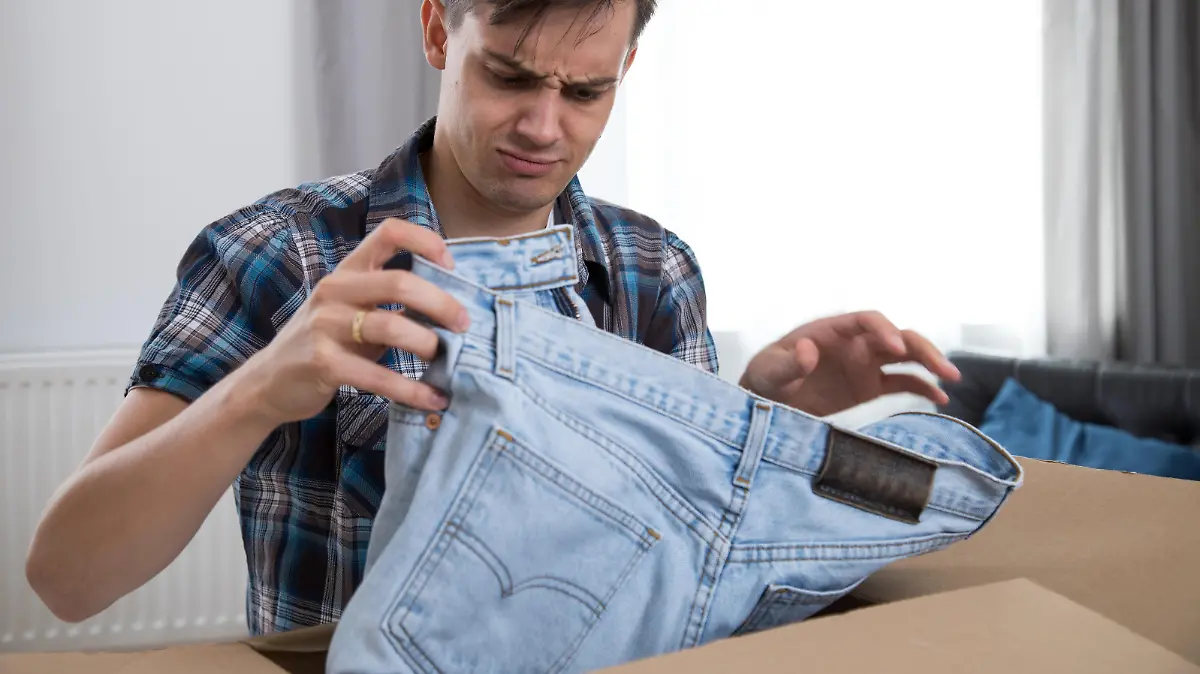 ILLUSTRATION - Ein junger Mann oeffnet am 14.09.2018 in Hamburg ein Paket und nimmt eine Jeans raus (gestellte Szene). Foto: Christin Klose