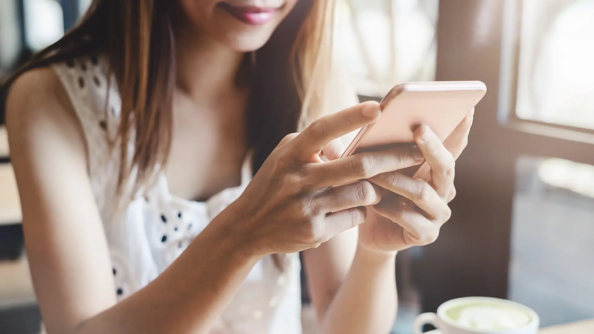 Eine Junge Frau sitzt an einem Kaffeetisch und verwendet ihr Handy. 