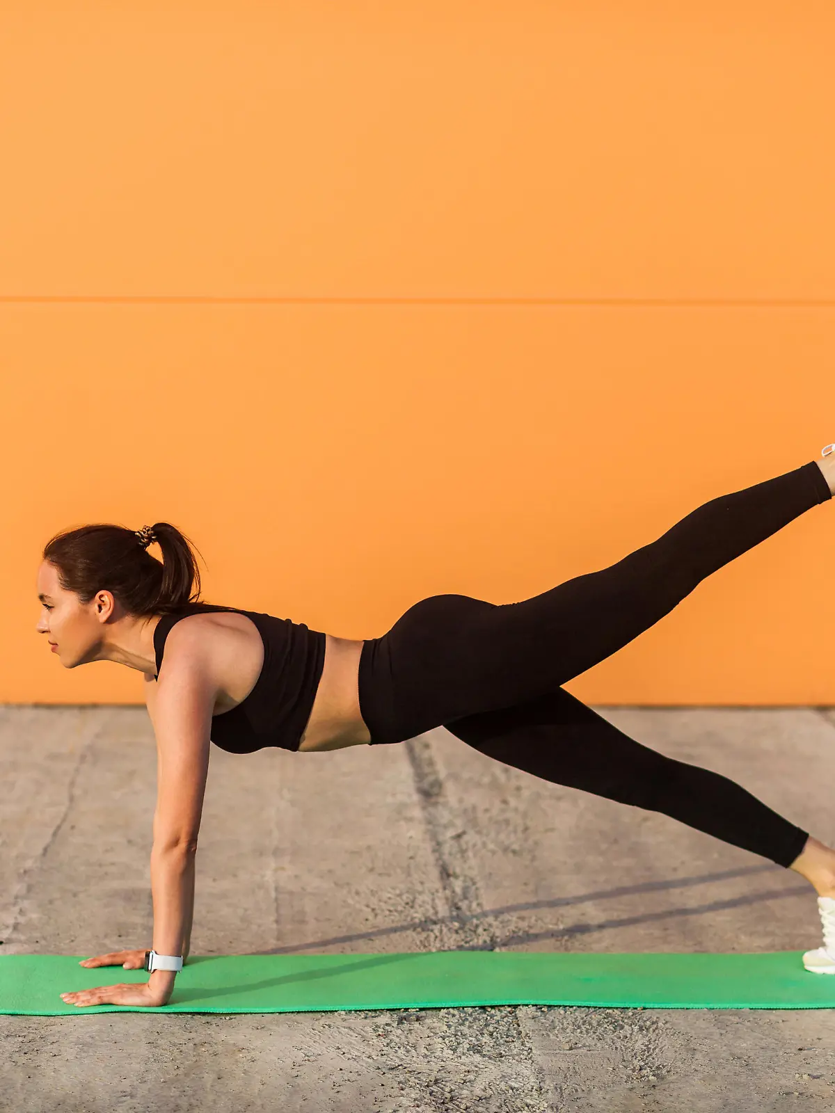 Eine junge, sportliche Frau in Sportkleidung führt eine Fitness-Übung auf ihrer Yogamatte durch.