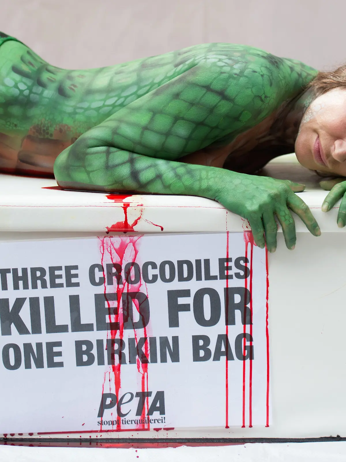 Mit einem Krokodil-Bodypainting auf ihrem ganzen Körper liegt die Schauspielerin Alexandra Kamp bei einer Peta-Protestaktion gegen Luxus-Handtaschen aus Krokodilleder der französischen Edelmarke Hermes am 26.08.2015 vor dem Hermès-Store am Neuen Wall in Hamburg. Unter ihr liest man auf einem Transparent: "Three crocodiles killed for one Birkin Bag". Foto: Daniel Reinhardt/dpa +++(c) dpa - Bildfunk+++