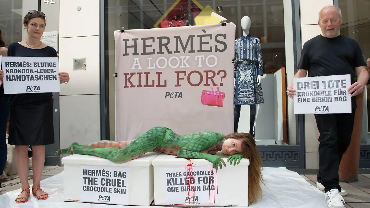 Mit einem Krokodil-Bodypainting auf ihrem ganzen Körper liegt die Schauspielerin Alexandra Kamp bei einer Peta-Protestaktion gegen Luxus-Handtaschen aus Krokodilleder der französischen Edelmarke Hermes am 26.08.2015 vor dem Hermès-Store am Neuen Wall in Hamburg. Neben ihr liest man auf Transparenten (l-r): "Hermes: Blutige Krokodil-Leder-Handtaschen", "Hermès a look to kill for?" und "Drei tote Krokodile für eine Birkin Bag". Foto: Daniel Reinhardt/dpa +++(c) dpa - Bildfunk+++