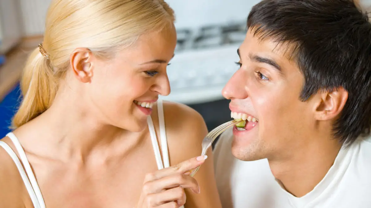 Funny scene of young happy couple playfully eating at kitchen