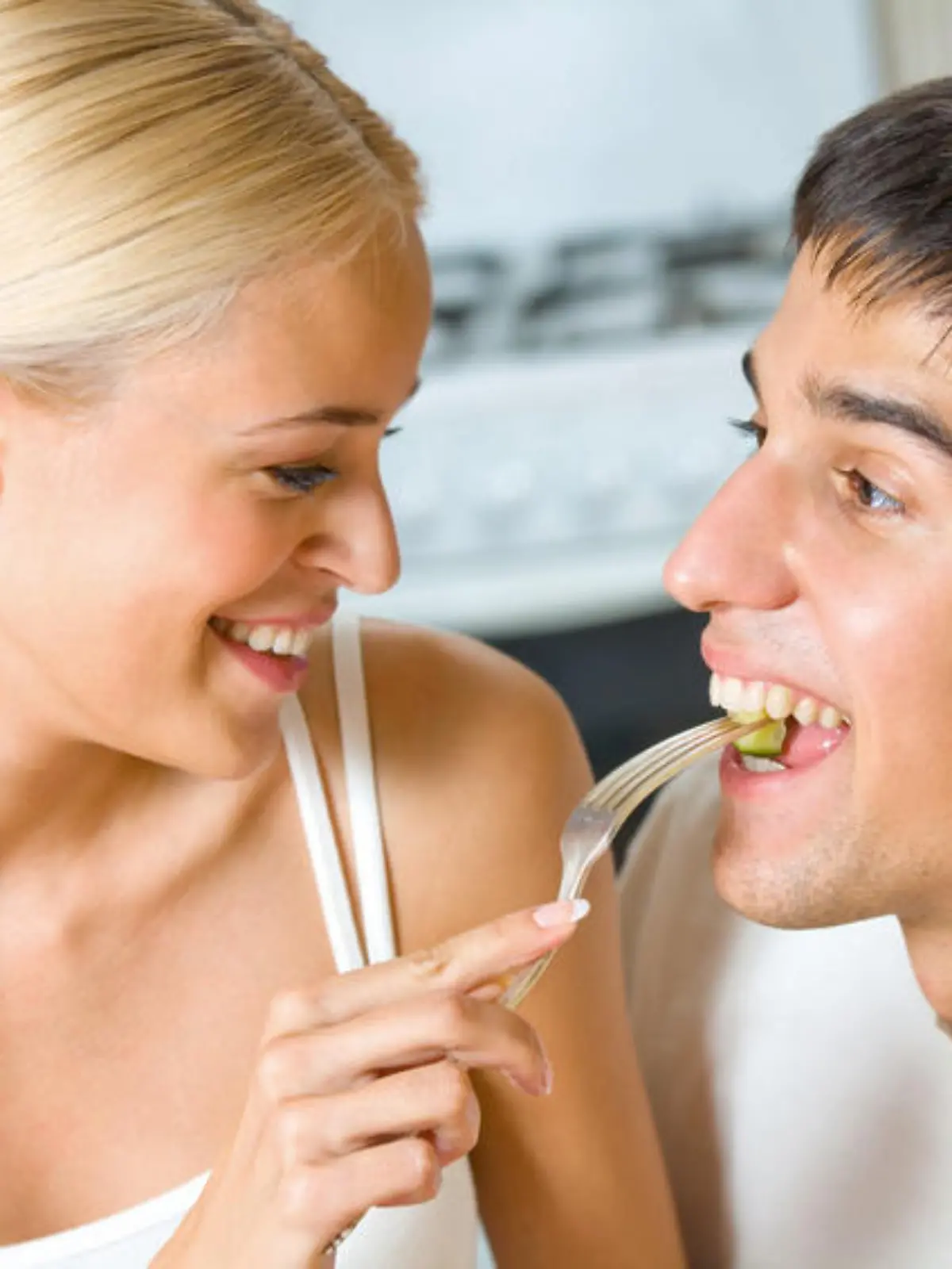 Funny scene of young happy couple playfully eating at kitchen