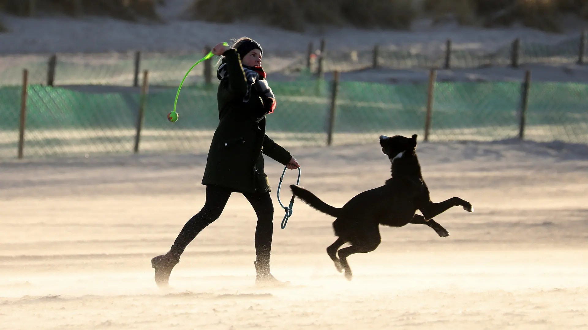 21.01.2021, Mecklenburg-Vorpommern, Warnemünde: Eine Frau ist mit ihrem Hund am Ostseestrand unterwegs, im schrägen Licht der aufgehenden Sonne leuchtet der Sand hell. Nach dem tagelangen Schmuddelwetter mit Regen und Schnee ist sie ein seltener Gast geworden. Foto: Bernd Wüstneck/dpa-Zentralbild/dpa +++ dpa-Bildfunk +++