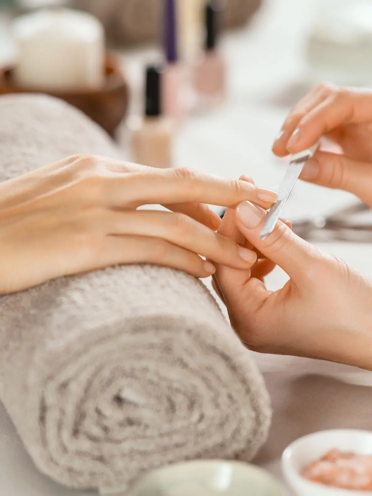 Close up shot of a woman in a nail salon receiving manicure by beautician with metal nail file. Woman getting nail manicure at spa centre. Beautician file nails to a customer in luxury salon.