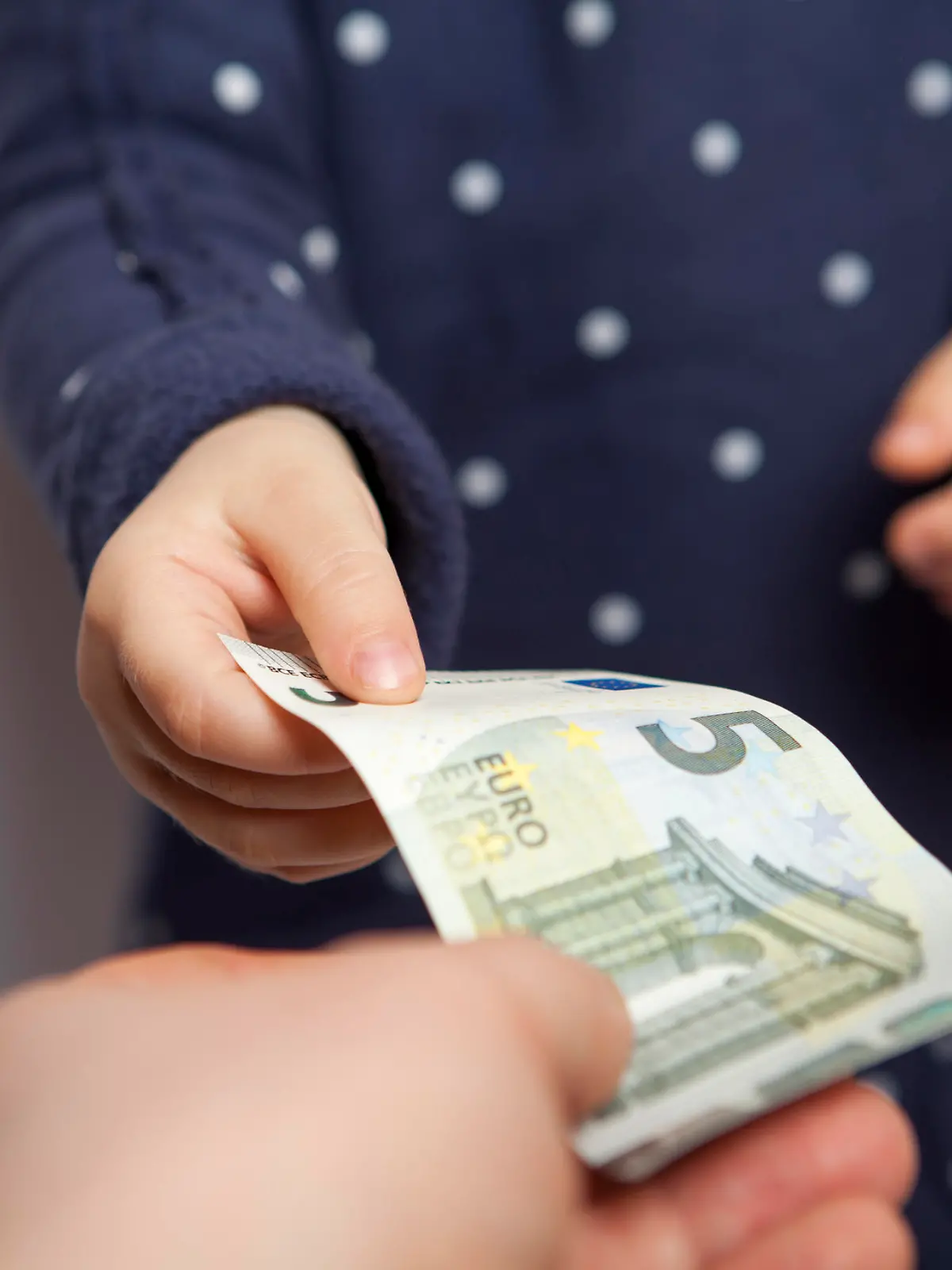 Small child hand takes five euros banknote from adult hand
