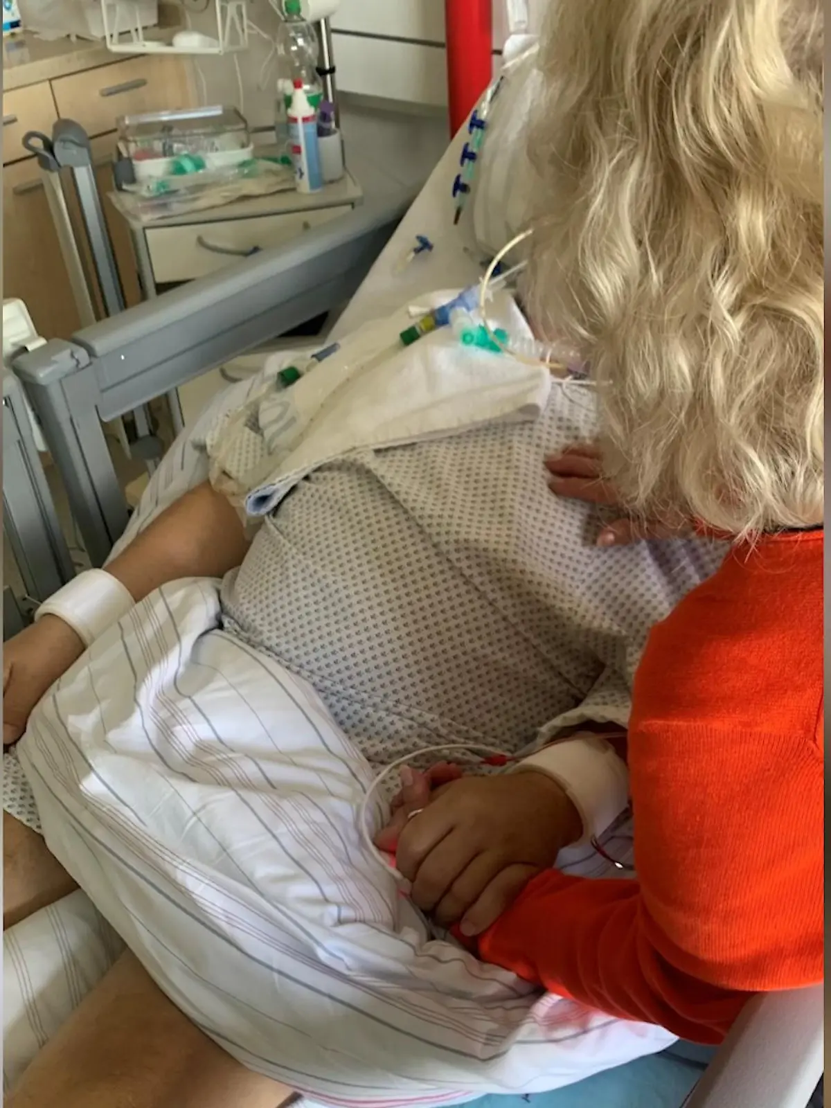 Ein Mann im Krankenbett, im Vordergrund sieht man eine Frau von hinten.