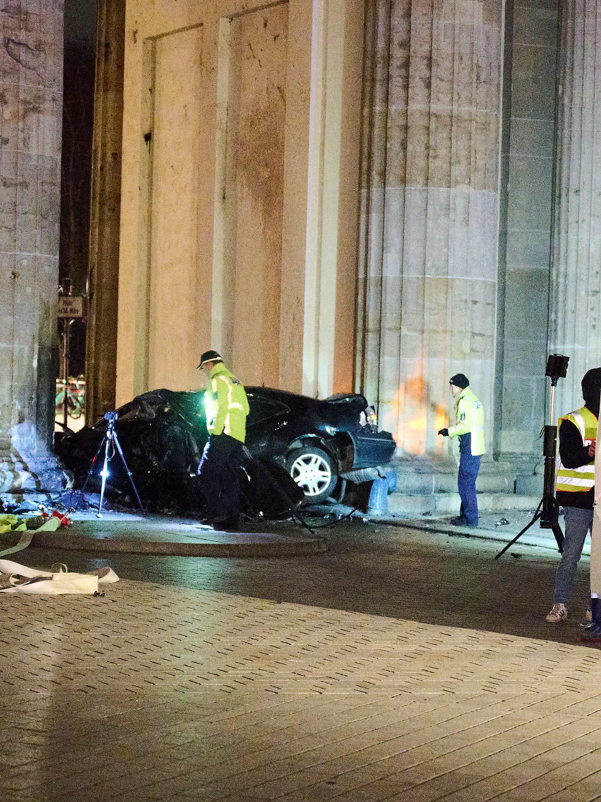 16.01.2023, Berlin: Ein zerstörter PKW liegt zwischen zwei Säulen des Brandenburger Tors während Einsatzkräfte der Polizei ermitteln. Ein Auto ist gegen eine Säule des Brandenburger Tors in Berlin gefahren. In dem Wagen hätten Feuerwehrleute einen toten Mann gefunden, sagte ein Polizeisprecher am frühen Montagmorgen. Foto: Annette Riedl/dpa +++ dpa-Bildfunk +++