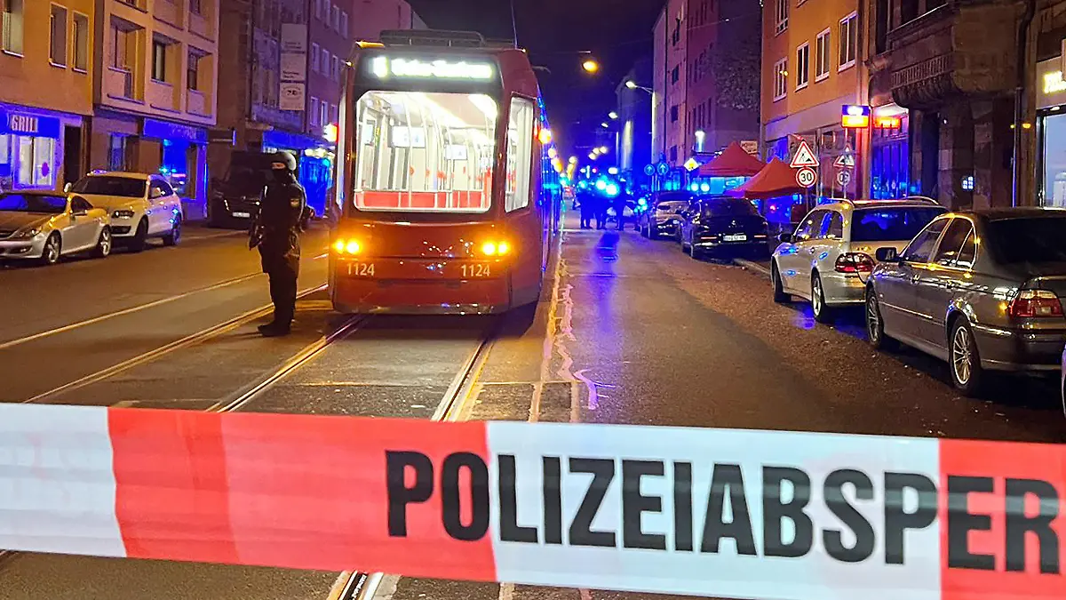 24.10.2022, Bayern, Nürnberg: Ein Polizist steht mit einer Maschinenpistole neben einer Straßenbahn hinter einer Polizeiabsperrung. Bei Schüssen in der Nürnberger Südstadt sind am Montagabend zwei Menschen schwer verletzt worden. Gegen 20.00 Uhr habe es eine gewaltsame Auseinandersetzung zwischen mehreren Personen gegeben, teilte ein Sprecher der Polizei am Abend auf Nachfrage mit. Hierbei seien nach ersten Erkenntnissen mehrere Schüsse abgegeben und dabei zwei Menschen schwer verletzt worden. Foto: Eberlein/vifogra/dpa +++ dpa-Bildfunk +++