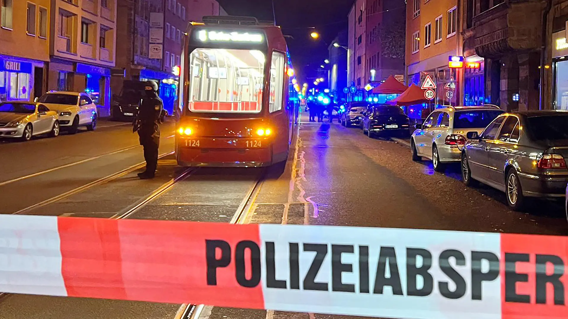 24.10.2022, Bayern, Nürnberg: Ein Polizist steht mit einer Maschinenpistole neben einer Straßenbahn hinter einer Polizeiabsperrung. Bei Schüssen in der Nürnberger Südstadt sind am Montagabend zwei Menschen schwer verletzt worden. Gegen 20.00 Uhr habe es eine gewaltsame Auseinandersetzung zwischen mehreren Personen gegeben, teilte ein Sprecher der Polizei am Abend auf Nachfrage mit. Hierbei seien nach ersten Erkenntnissen mehrere Schüsse abgegeben und dabei zwei Menschen schwer verletzt worden. Foto: Eberlein/vifogra/dpa +++ dpa-Bildfunk +++