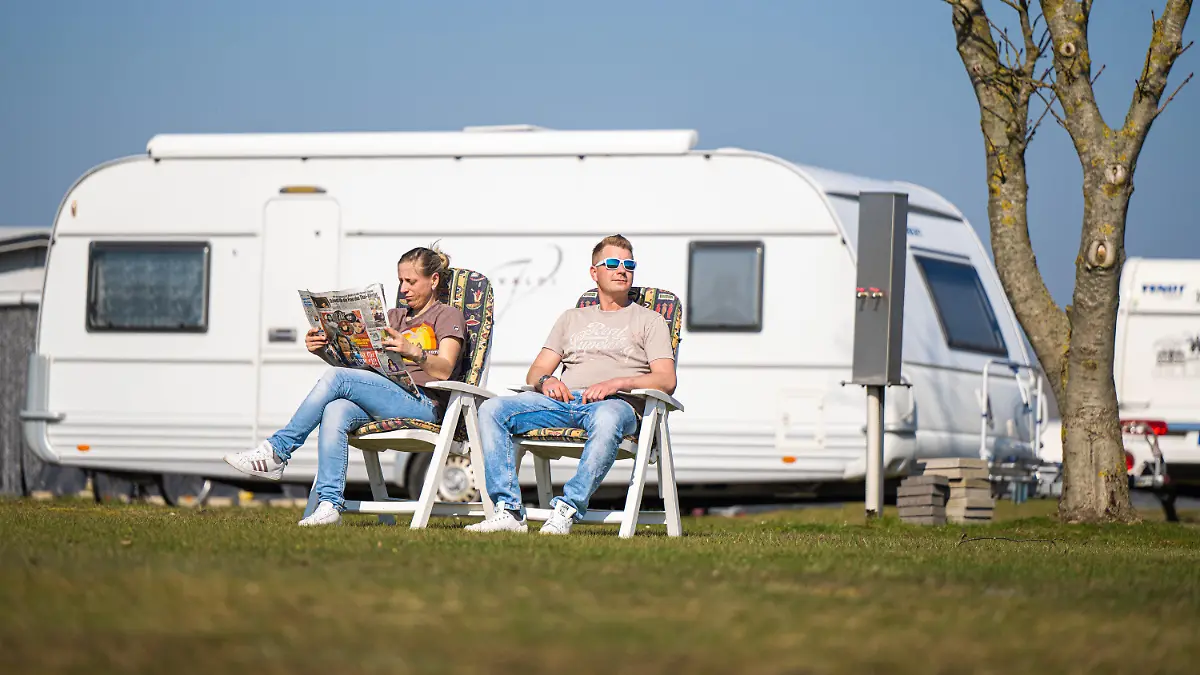 31.03.2021, Niedersachsen, Hooksiel: Die Dauercamper Nadine und Marcel aus Nordrhein-Westfalen sitzen vor einem Wohnwagen auf dem Campingplatz von Hooksiel, wo sie bis Oktober ihren Aufenthalt geplant haben. Sie sind bereits das dritte Jahr in Folge auf dem Platz. Foto: Mohssen Assanimoghaddam/dpa +++ dpa-Bildfunk +++