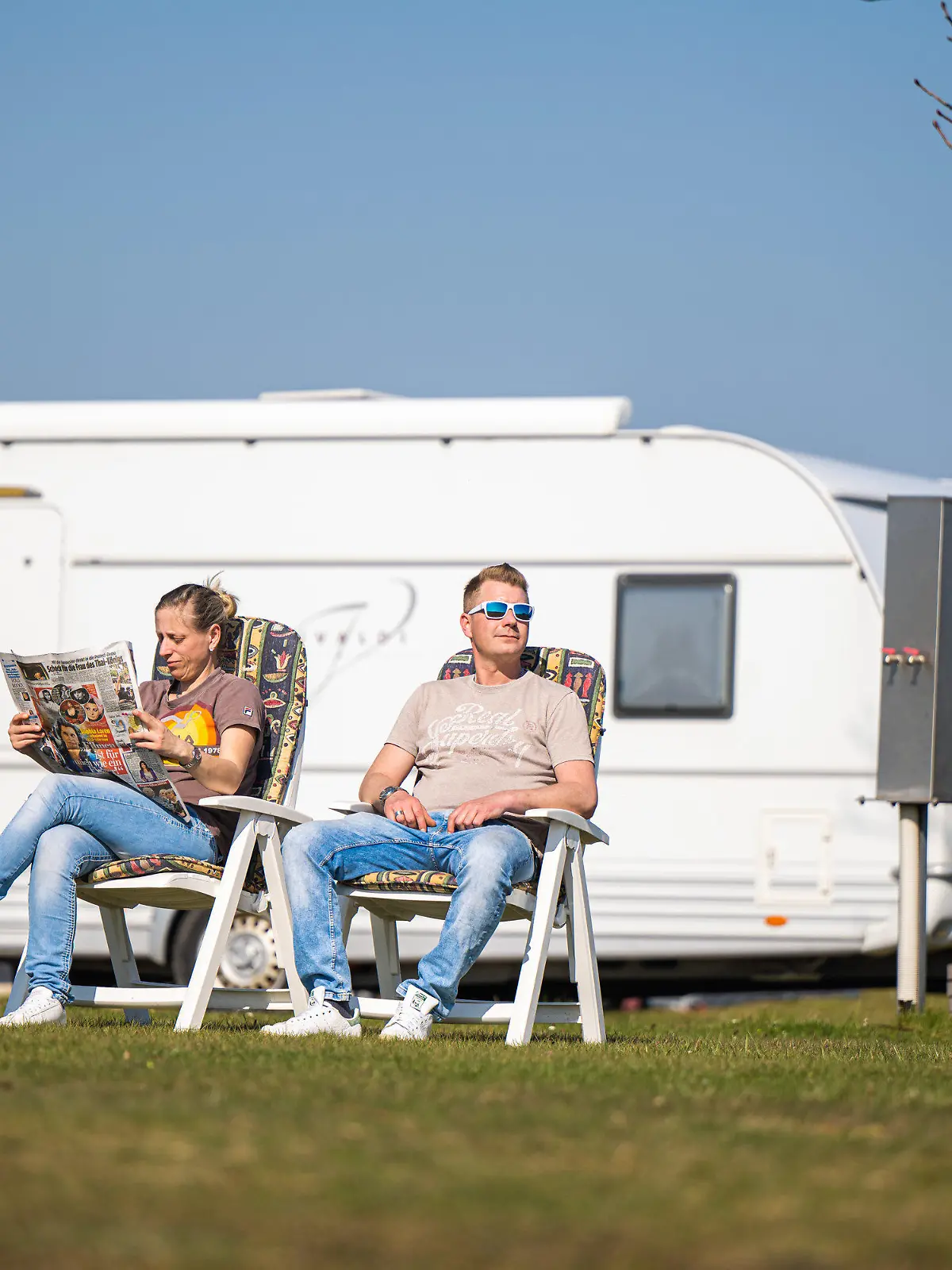 31.03.2021, Niedersachsen, Hooksiel: Die Dauercamper Nadine und Marcel aus Nordrhein-Westfalen sitzen vor einem Wohnwagen auf dem Campingplatz von Hooksiel, wo sie bis Oktober ihren Aufenthalt geplant haben. Sie sind bereits das dritte Jahr in Folge auf dem Platz. Foto: Mohssen Assanimoghaddam/dpa +++ dpa-Bildfunk +++