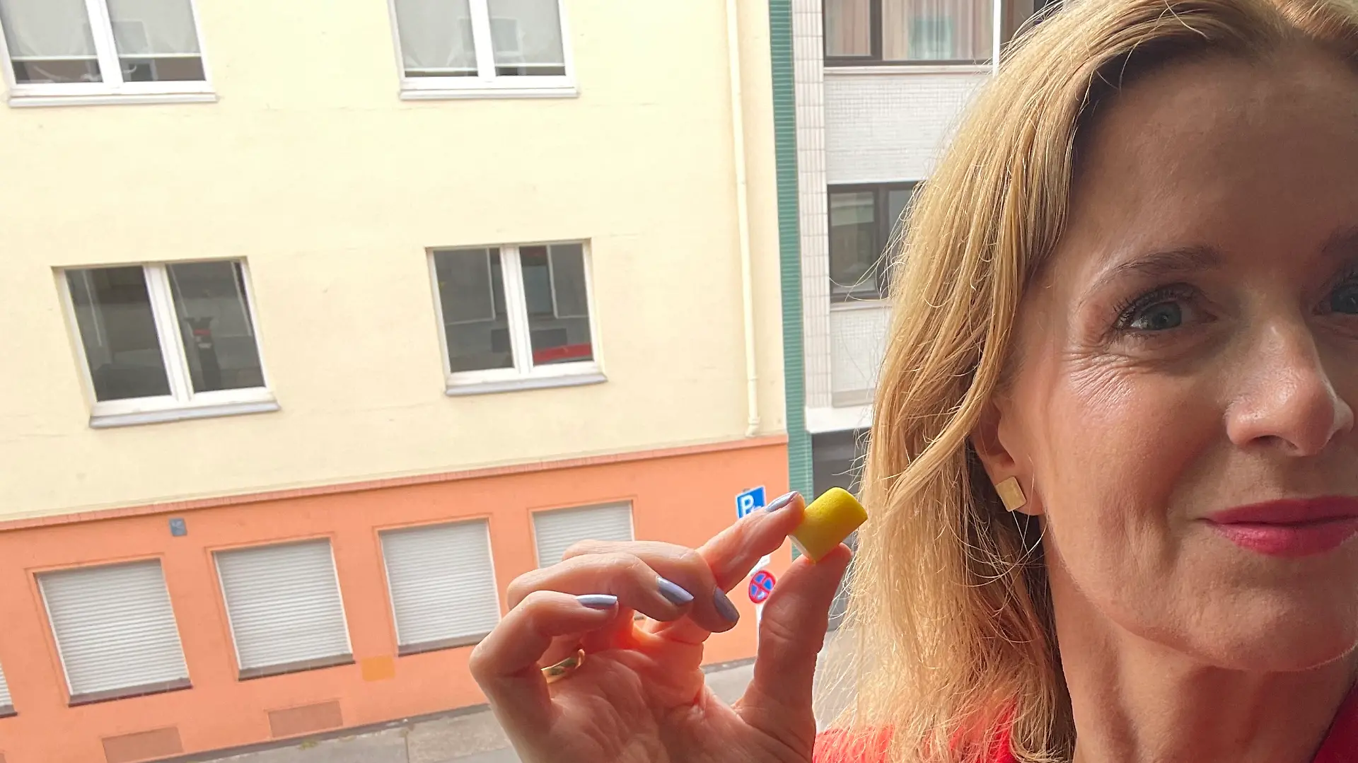 Redakteurin Maren Mangold zeigt 3M Ohrstöpsel neben ihrem Ohr vor einem Fenster Richtung Straße.