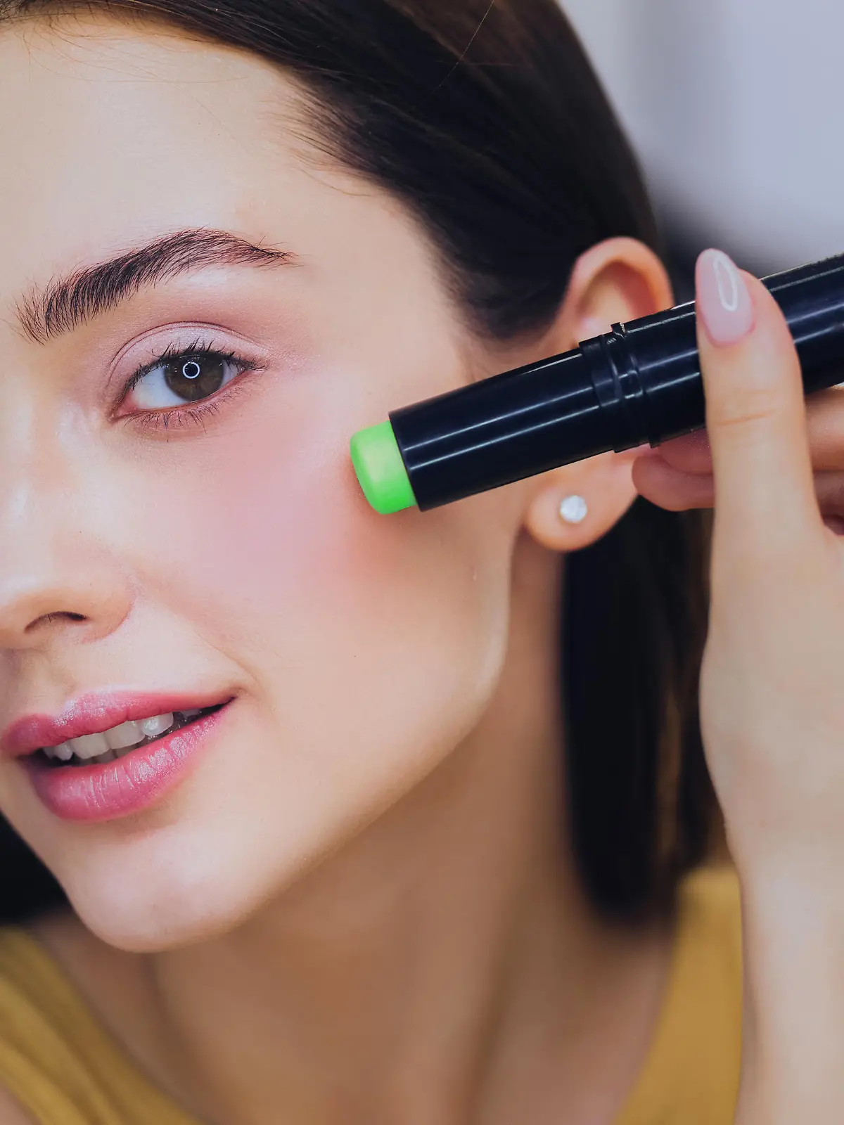 Frau trägt grünen Concealer mit Korrekturstift auf.