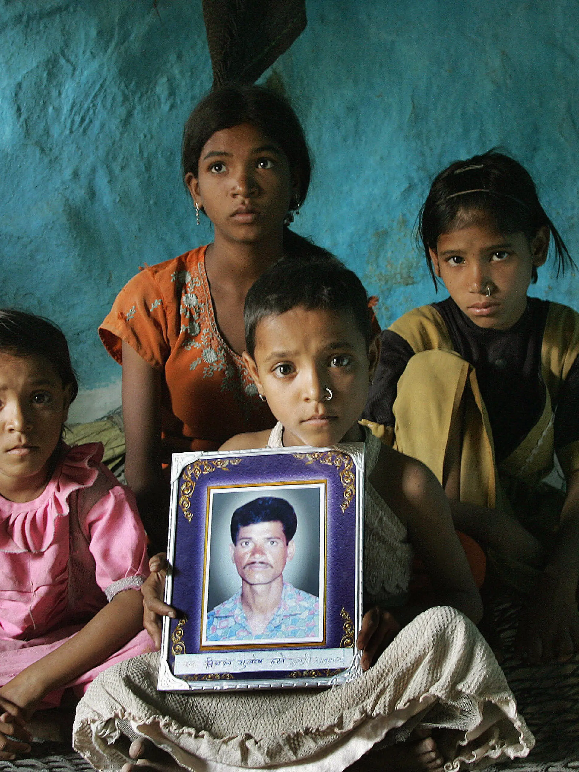 Yavatmal, INDIA:  (FILES) In this picture taken 18 April 2006, the four daughters of the late Indian cotton farmer Neelkhant Haste: Pranali (L), Seema (2L), Ruchali (3L), and Kajol (R) pose with his picture as they mourn his death at Yavatmal on the outskirts of Nagpur, after he committed suicide by consuming pesticide.   Farmer suicides in India's main cotton belt have reached their highest ever level with 216 dead since premier Manmohan Singh announced a major relief effort in July, community leaders said 04 September 2006.  The monthly death toll hit more than 100 for the first time in August and suicides are continuing at three a day among farmers hit hard by rising debt and falling cotton prices.Tallies compiled by activists show 767 farmers killed themselves in the last 12 months in the Vidarbha region in western Maharashtra state, with many setting themselves alight or drinking pesticide. Activists say only a few hundred farmers have been helped by Singh's 37.5-billion rupee (835 million USD) relief package announced after a two-day visit to Vidarbha.   AFP PHOTO/Sebastian D'SOUZA/FILES  (Photo credit should read SEBASTIAN D'SOUZA/AFP/Getty Images)