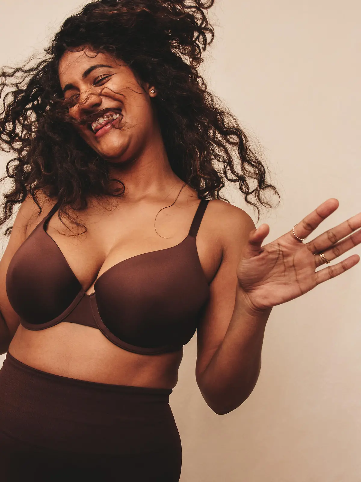 Filled with happiness and positive vibes. Happy young woman laughing cheerfully while standing against a studio background. Body positive young woman embracing her natural self.