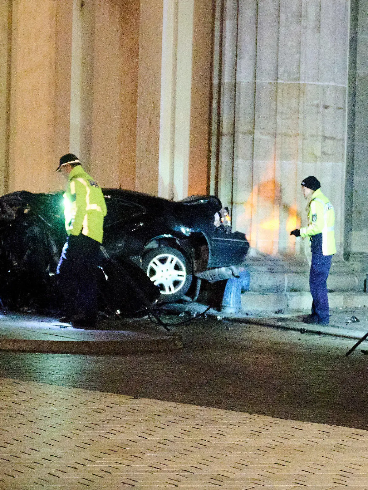 16.01.2023, Berlin: Ein zerstörter PKW liegt zwischen zwei Säulen des Brandenburger Tors während Einsatzkräfte der Polizei ermitteln. Ein Auto ist gegen eine Säule des Brandenburger Tors in Berlin gefahren. In dem Wagen hätten Feuerwehrleute einen toten Mann gefunden, sagte ein Polizeisprecher am frühen Montagmorgen. Foto: Annette Riedl/dpa +++ dpa-Bildfunk +++