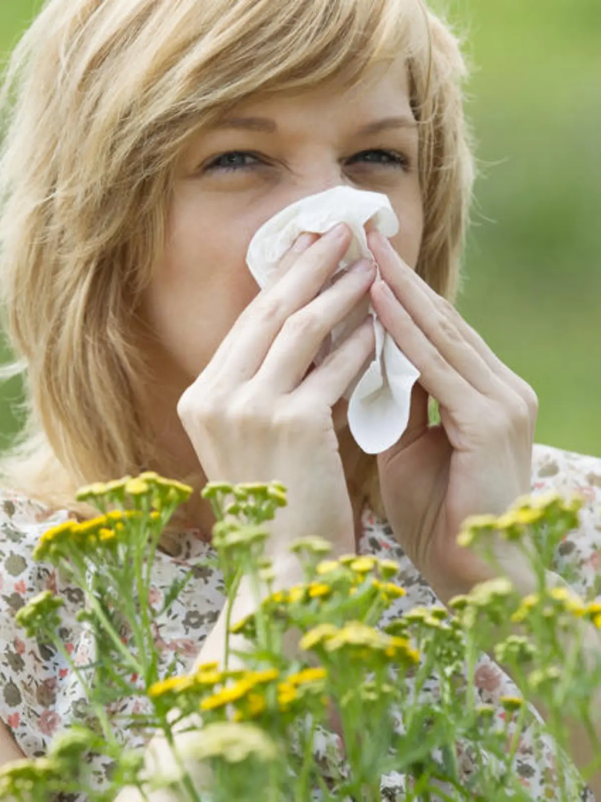 Young Caucasian woman blowing nose into tissue in front of flowers