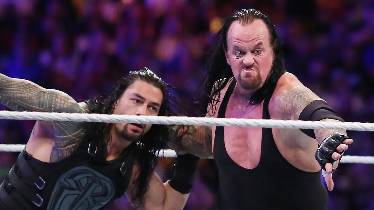 The Undertaker (rechts) mitten im Kampf. Hier schmeißt er Roman Reigns durch den Ring.