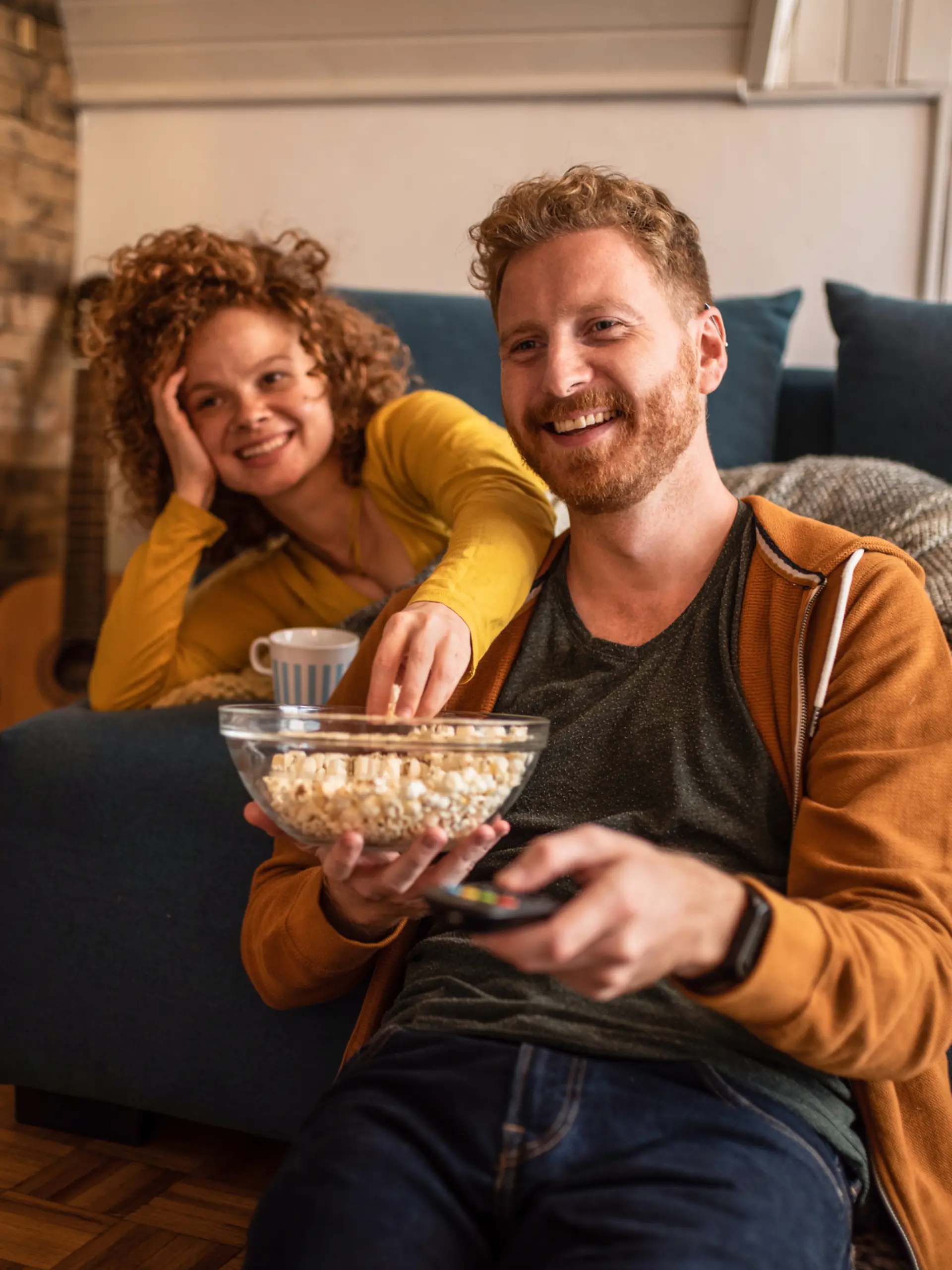 Ein Paar sitzt im Wohnzimmer vor dem Fernseher / schaut Fernsehen und hat Spaß