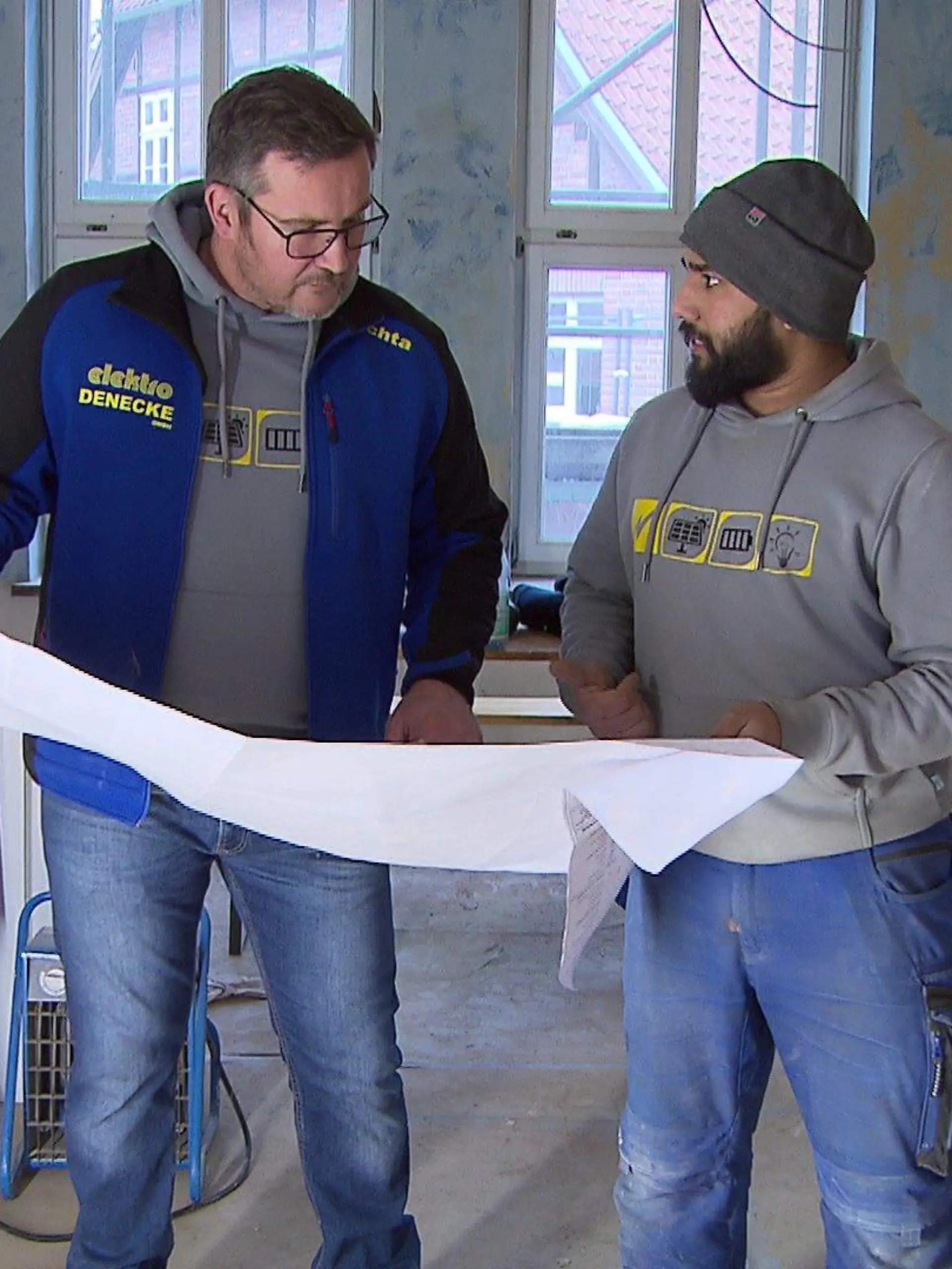 Azubi Sheraz Chaudhry und sein Meister Mathias Puchta begutachten auf der Baustelle Pläne.